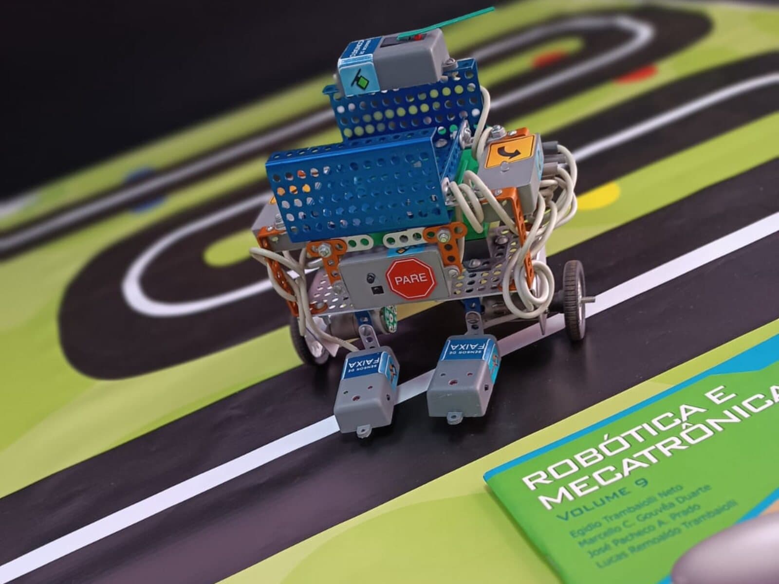 Robô ALPHA na pista, com os livros da coleção Robótica e Mecatrônica ao lado