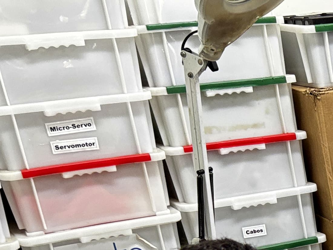Gavetas de componentes etiquetadas por tipo — micro-servo, servomotor e cabos — no estoque de produção