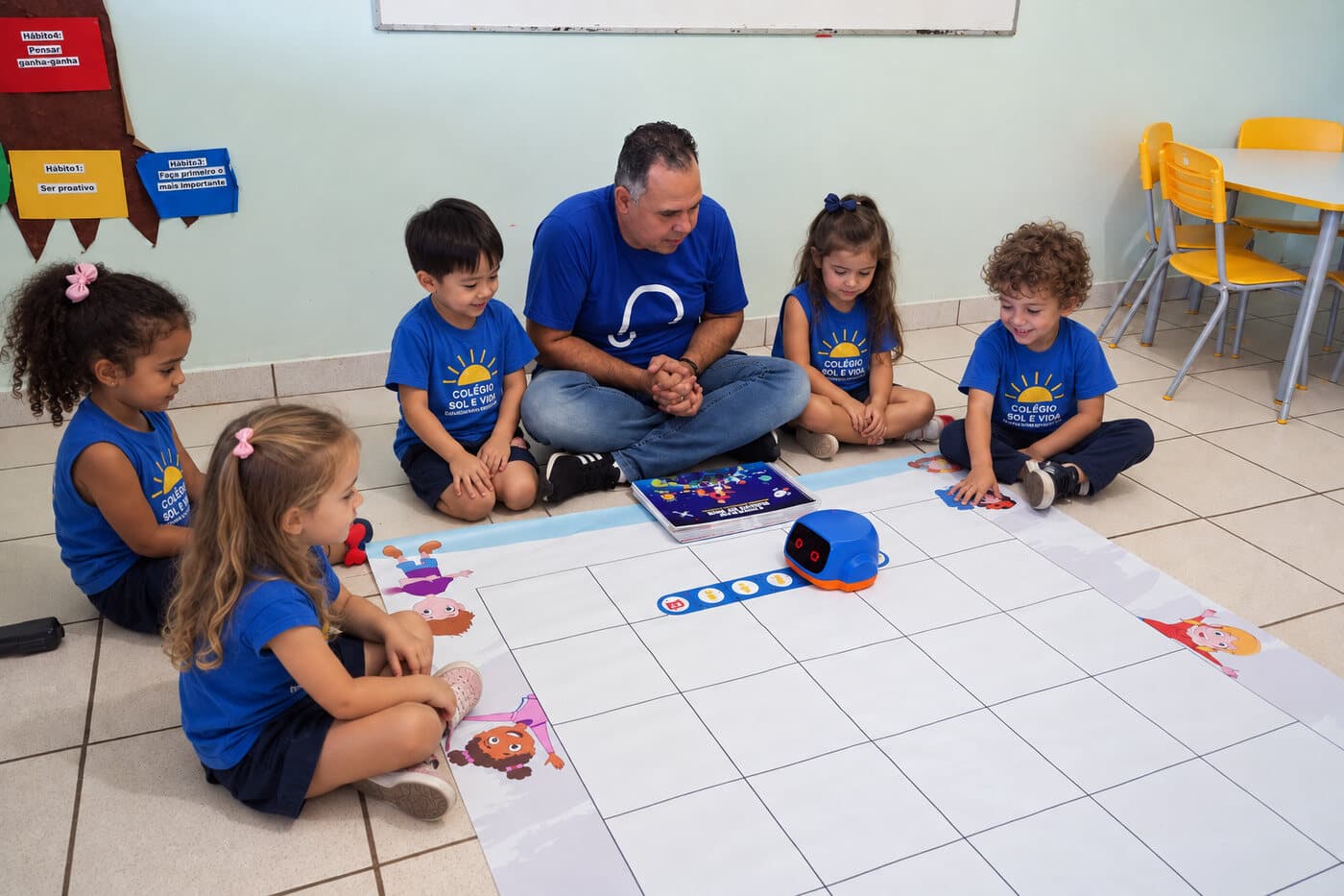 Turma da educação infantil em roda com o professor, executando a sequência de comandos com o ROB sobre o tapete